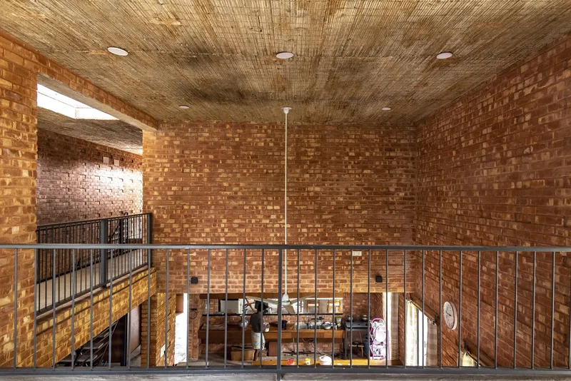 Upper level balcony with steel railing overlooking the living space below through a woven bamboo ceiling