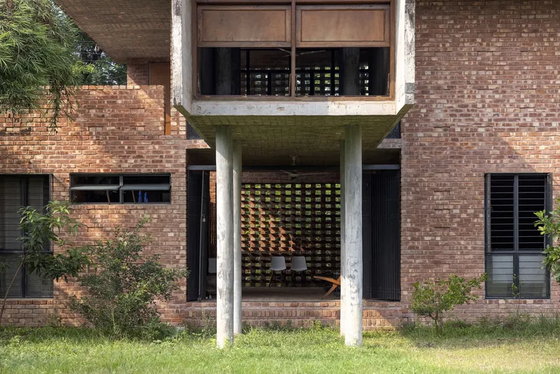Recessed entrance with cast concrete columns and perforated brick screen behind a green lawn