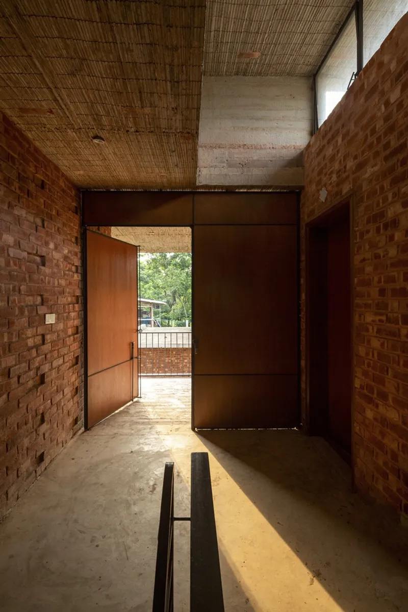 Entry corridor with pivoting timber door opening to sunlit courtyard framed by perforated brick walls