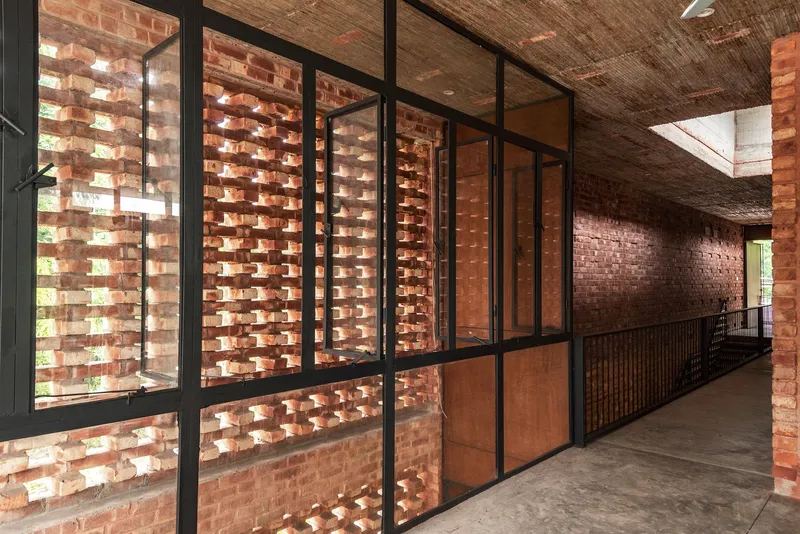 Interior corridor with steel-framed glazing adjacent to a perforated brick screen filtering daylight