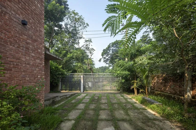 Grid of concrete pavers with grass growing between them leading to a metal gate