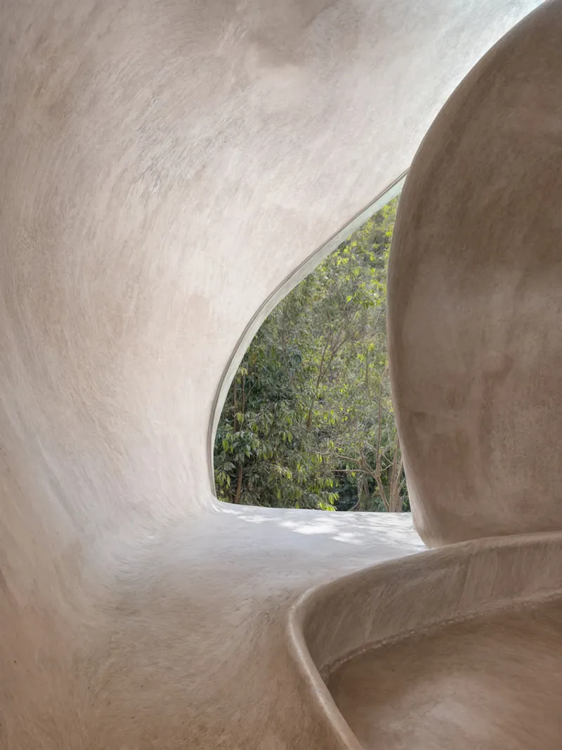 Curved plaster interior alcove with arched window opening framing dense tropical vegetation outside