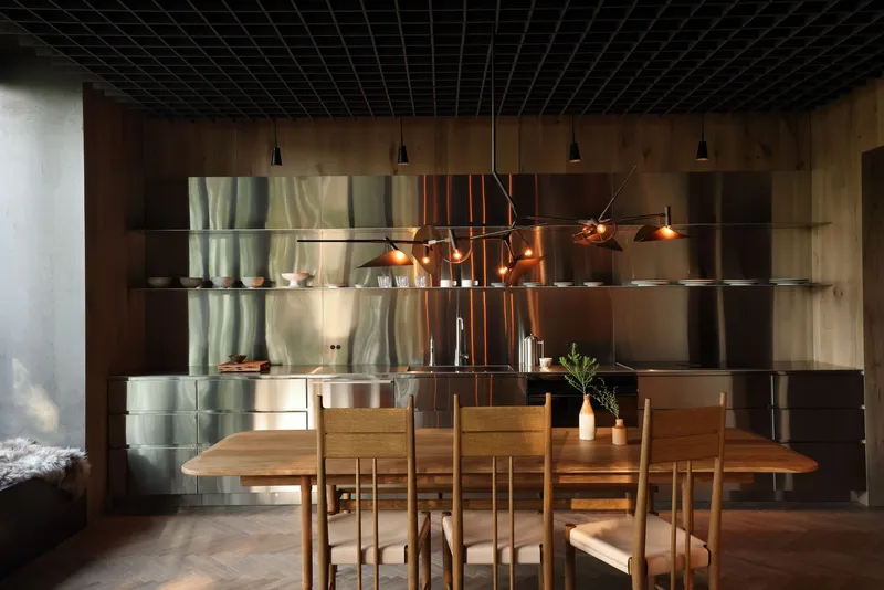 Dining area with stainless steel shelving wall and copper pendant lights beneath a black gridded ceiling