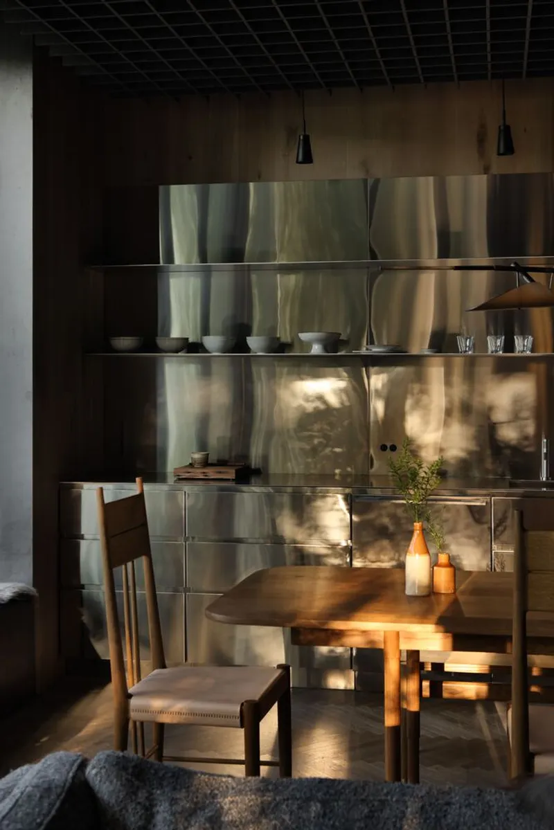 Stainless steel shelving unit displaying ceramics and glassware with dappled sunlight across its surface