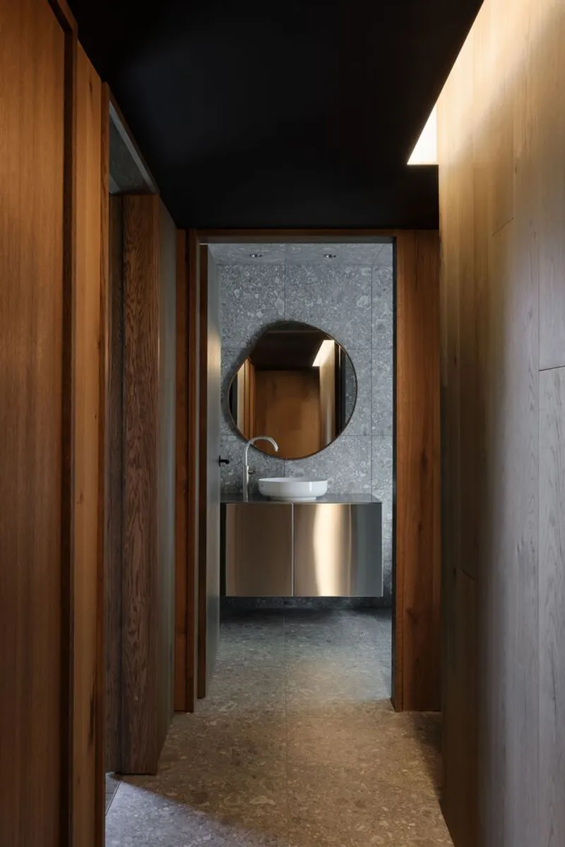 Corridor with timber walls leading to a bathroom with polished concrete and brass vanity