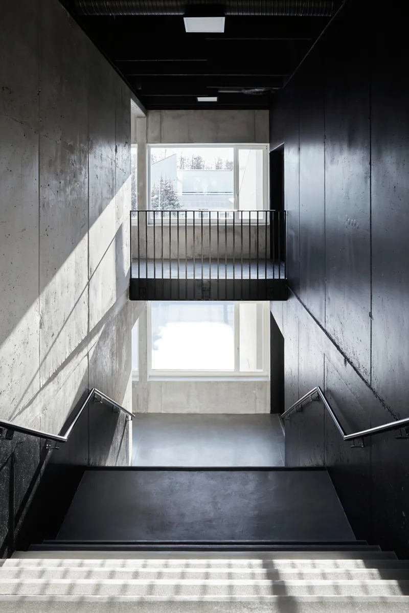 Stairwell with black metal railings and concrete walls illuminated by sunlight through windows