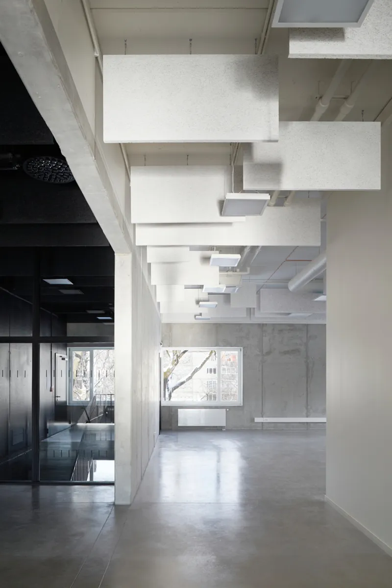 Open interior corridor with floating acoustic ceiling panels and concrete wall beside glazed partition