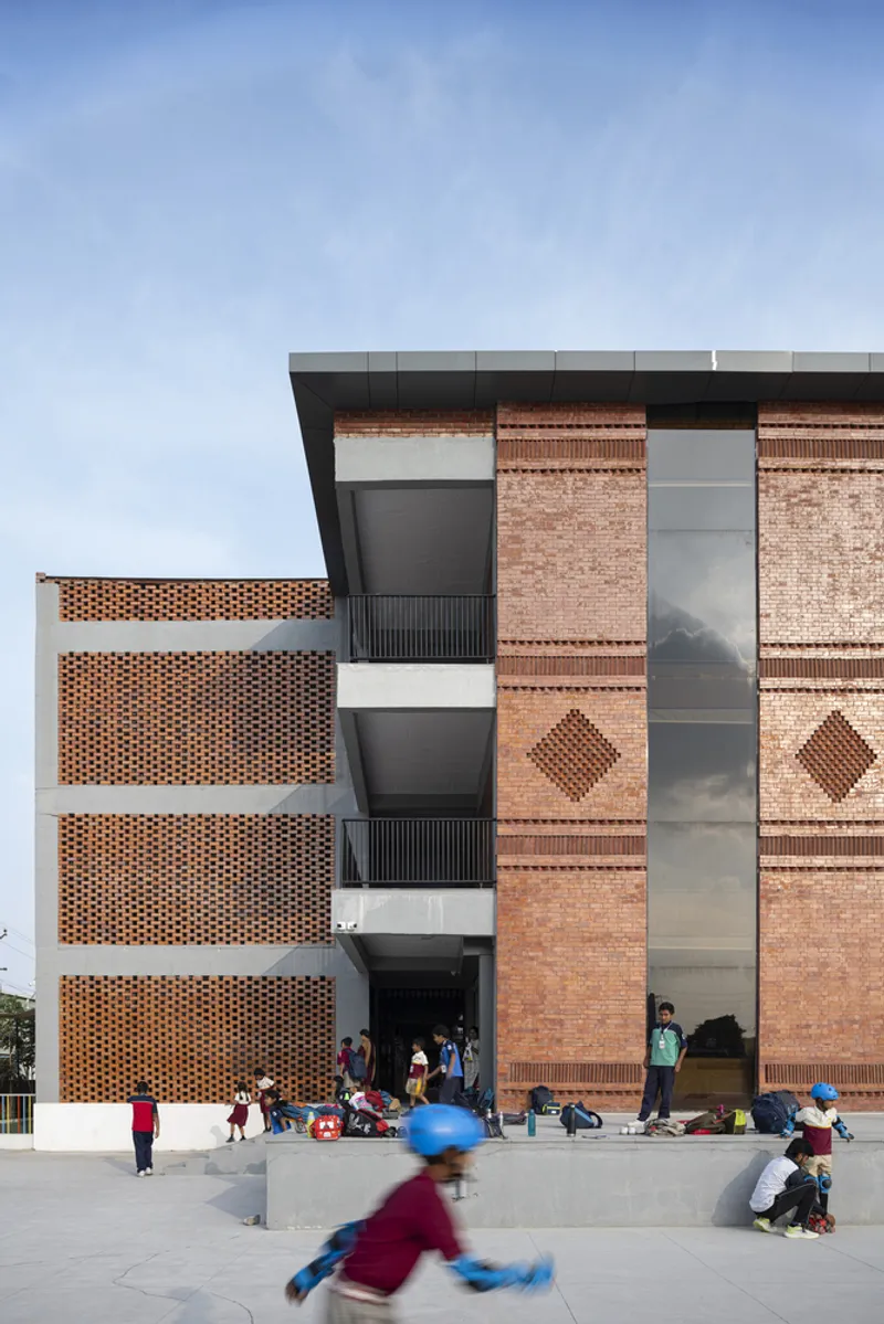 Facade combining patterned brick panels and perforated screens with children playing on the plaza below