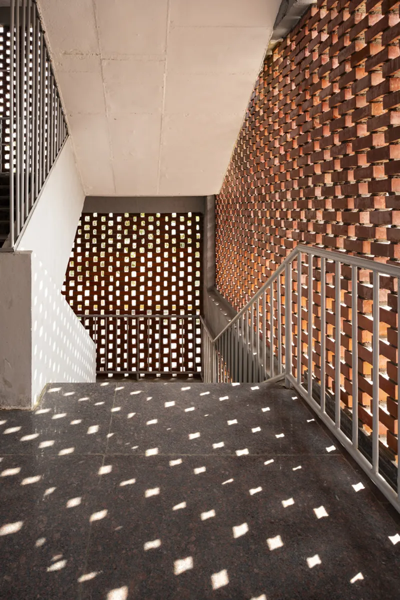 Stairwell with textured brick wall and perforated screen casting dappled sunlight on the landing