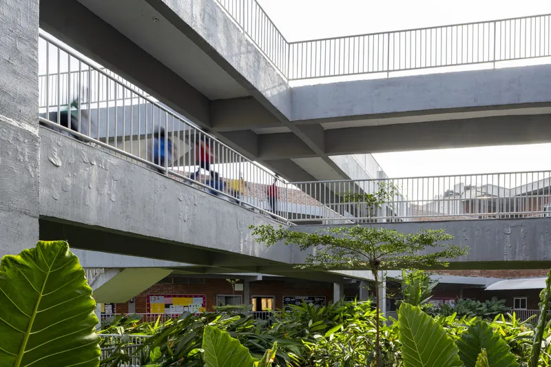 Stacked concrete walkways with metal railings crossing above a planted courtyard with young trees
