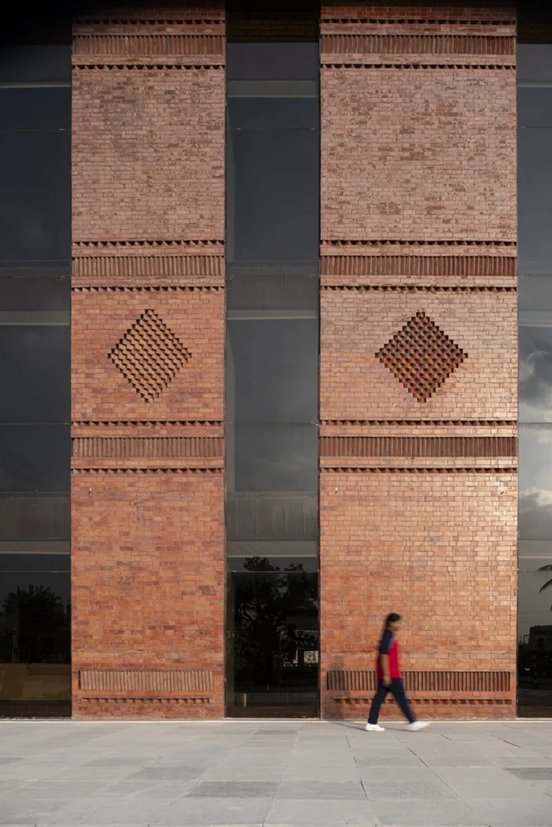Two brick columns with decorative corbelling and diamond patterns separated by a glass void as a figure walks past