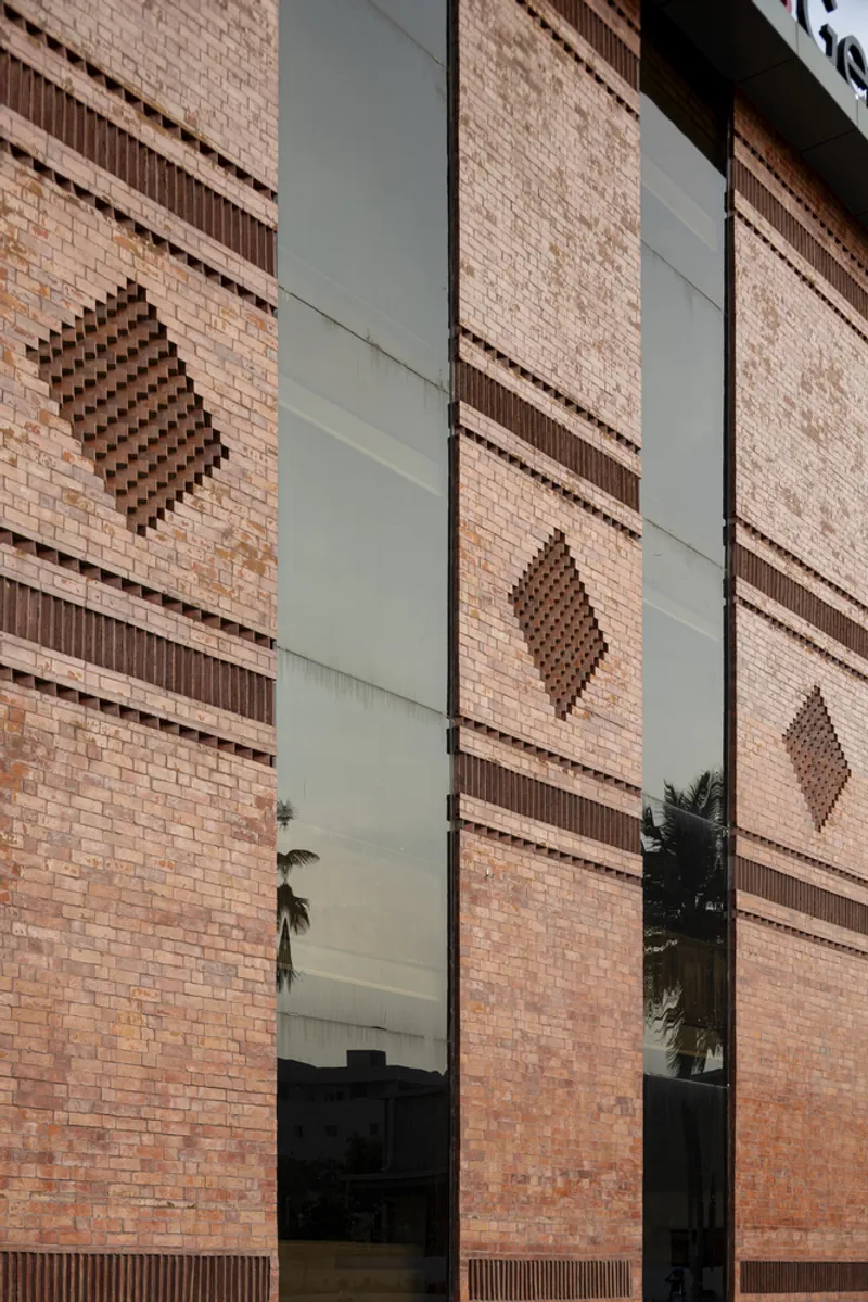 Close-up of patterned brick facade panels with diamond motifs flanking a vertical glass slot reflecting palm trees