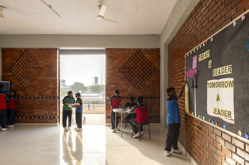 Classroom interior with patterned red brick walls and students gathered near the large opening to the courtyard