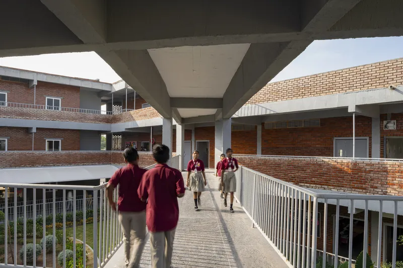 Elevated walkway with white metal railings connecting brick buildings as students cross under exposed concrete beams
