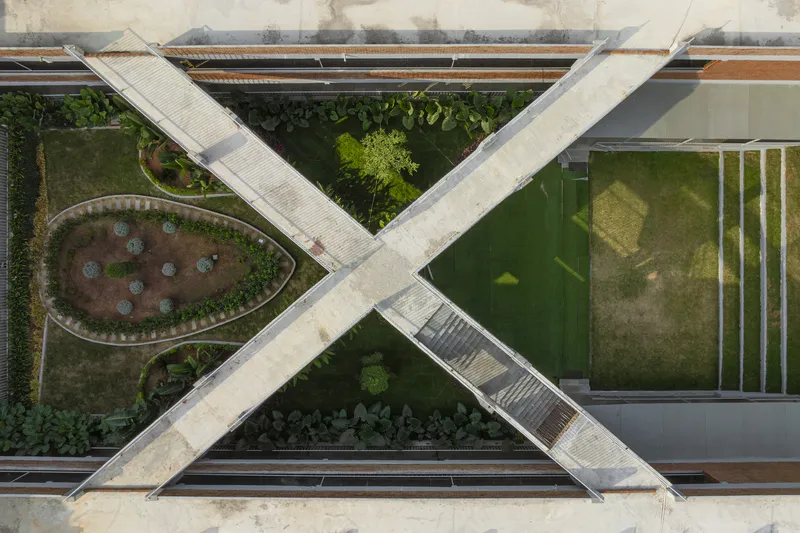 Aerial view of crossing concrete walkways forming an X over courtyard gardens and a glass-roofed sports court
