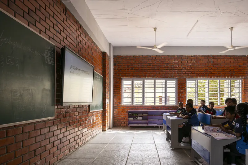 Classroom with exposed red brick walls and white louvered windows allowing natural light across the desks