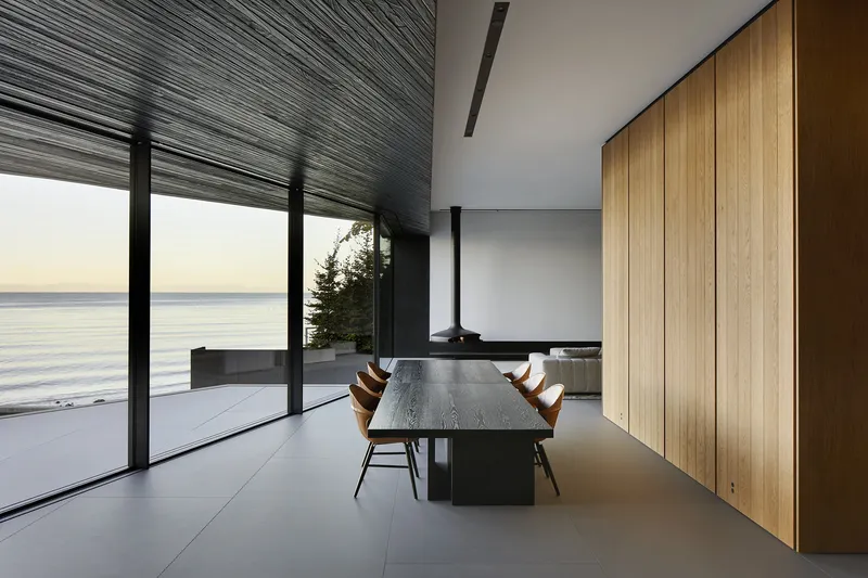 Interior dining space with timber paneling, glazed wall and ribbed ceiling at dusk
