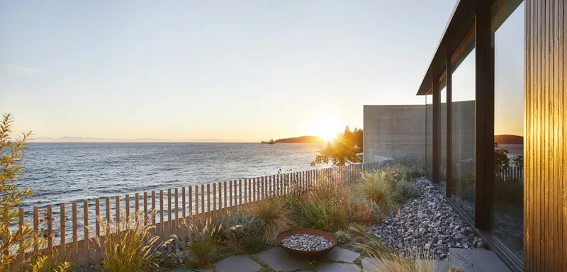 Waterfront terrace with gravel beds, grasses, and timber screen at sunset