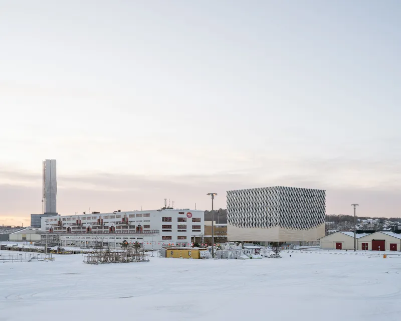 Winter view of the complex with a patterned facade volume and tower across a snow-covered field at dusk