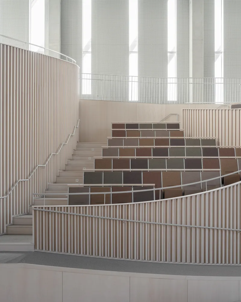 Curved staircase with vertical wood slat balustrade and colored tile risers beneath tall window columns