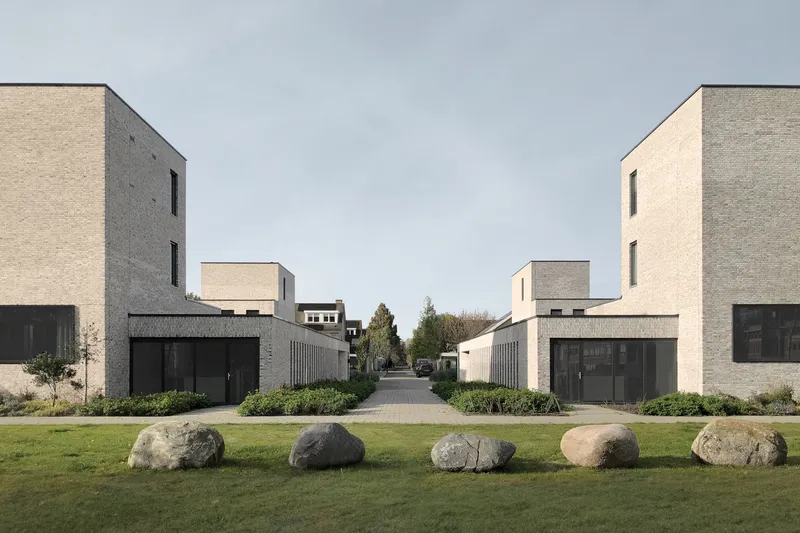 Symmetrical view of pale brick townhouses framing a central walkway with boulders on mown grass