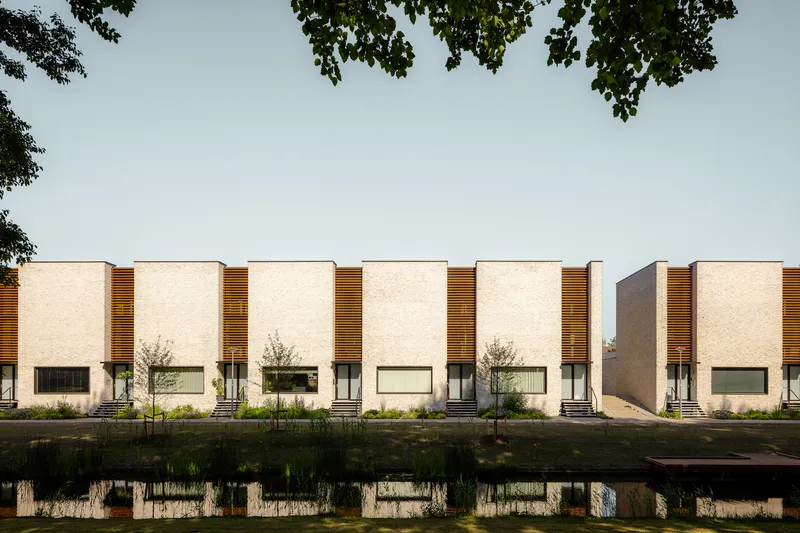 Repeating facade of cream brick units with timber slat screens reflected in a canal below