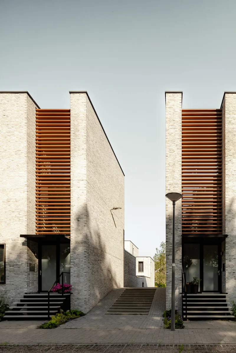 Twin entrances with metal staircases flanked by vertical timber slat screens on cream brick volumes