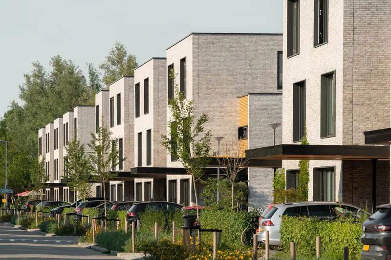 Streetscape of stepped brick housing blocks with young trees and parked cars along the curb