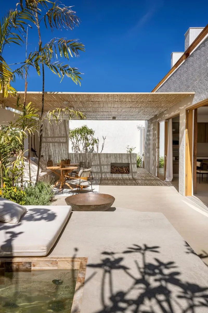Courtyard with woven reed pergola sheltering a timber dining table and shallow reflecting pool surrounded by palms
