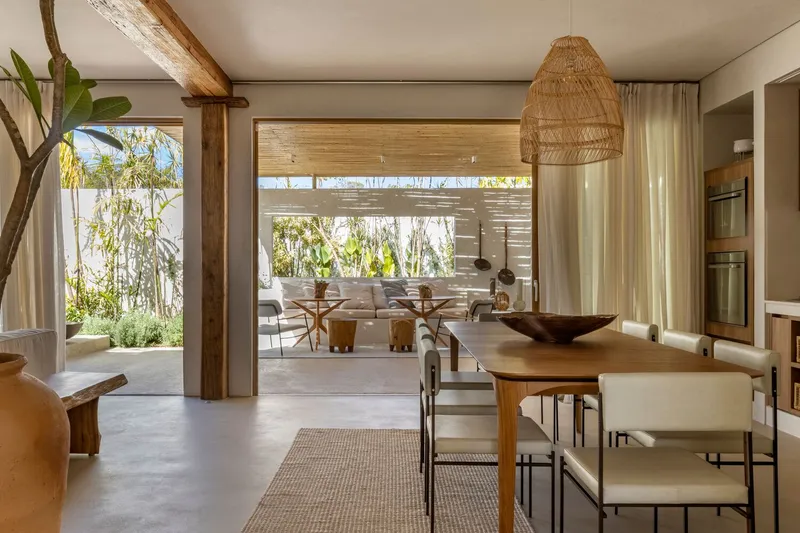 Open-plan dining area looking through to courtyard with timber beam, woven pendant light and concrete floor