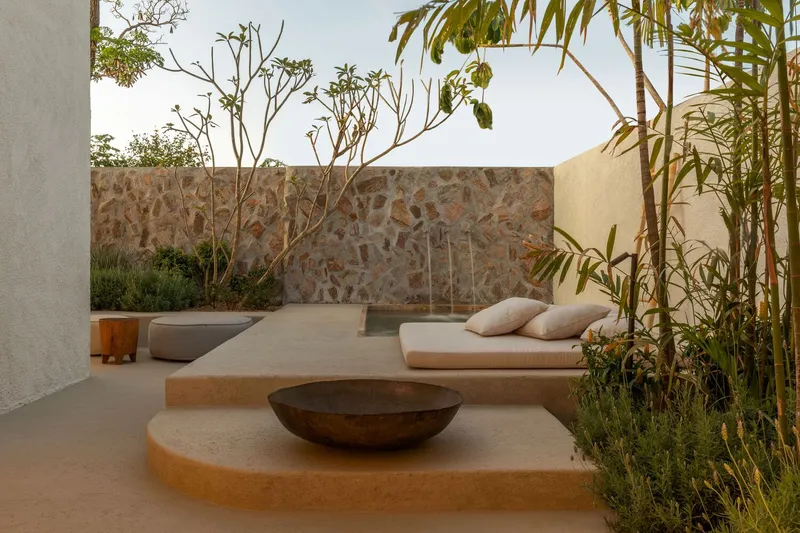 Courtyard with stone mosaic wall, built-in concrete seating, and planted trees in afternoon light