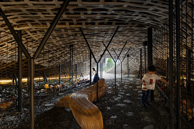 Interior space with woven lattice ceiling, steel bracing, bamboo benches, and visitors walking through on gravel floor