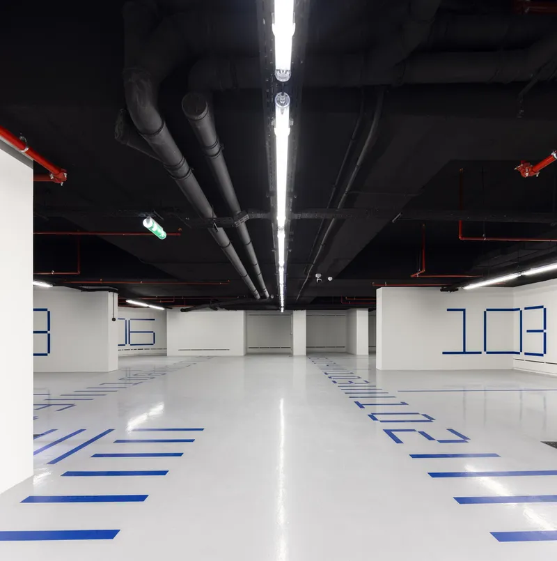 Underground parking garage with exposed black ceiling ducts and blue wayfinding graphics on white epoxy floor