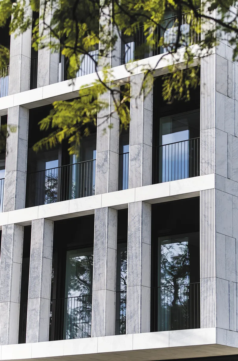 Facade detail showing recessed balconies with vertical ribbed stone panels and tree branches overhead