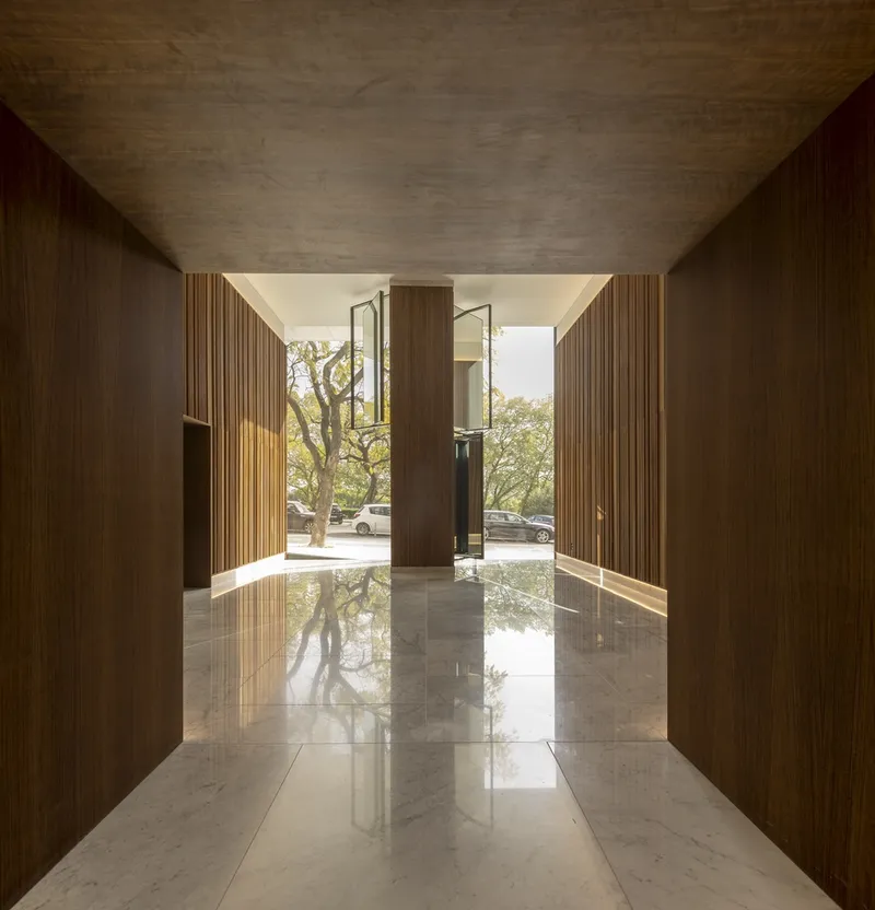 Entry corridor with vertical timber cladding and polished stone floor reflecting trees and sunlight beyond