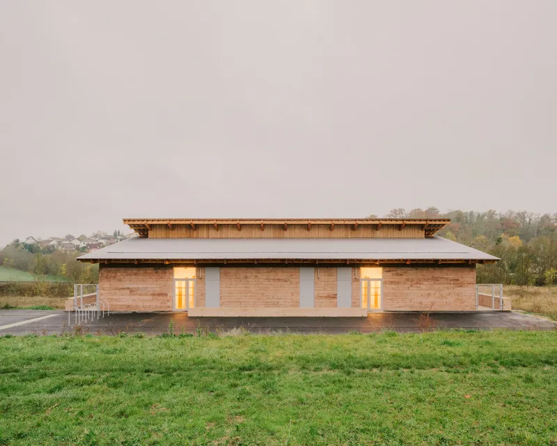 Facade with layered timber roof overhang and illuminated glass openings flanked by metal railings at dusk