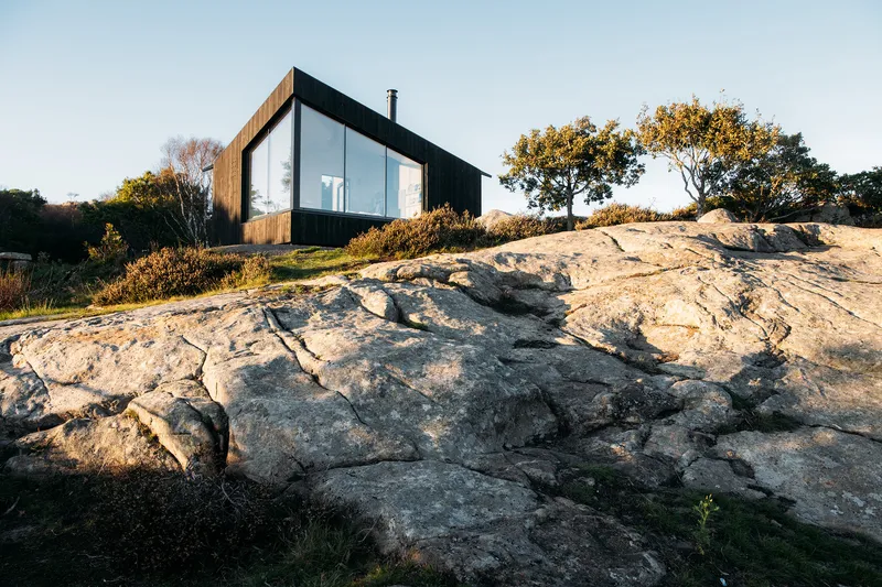 Glazed and timber-clad volume perched on exposed granite bedrock among autumn trees