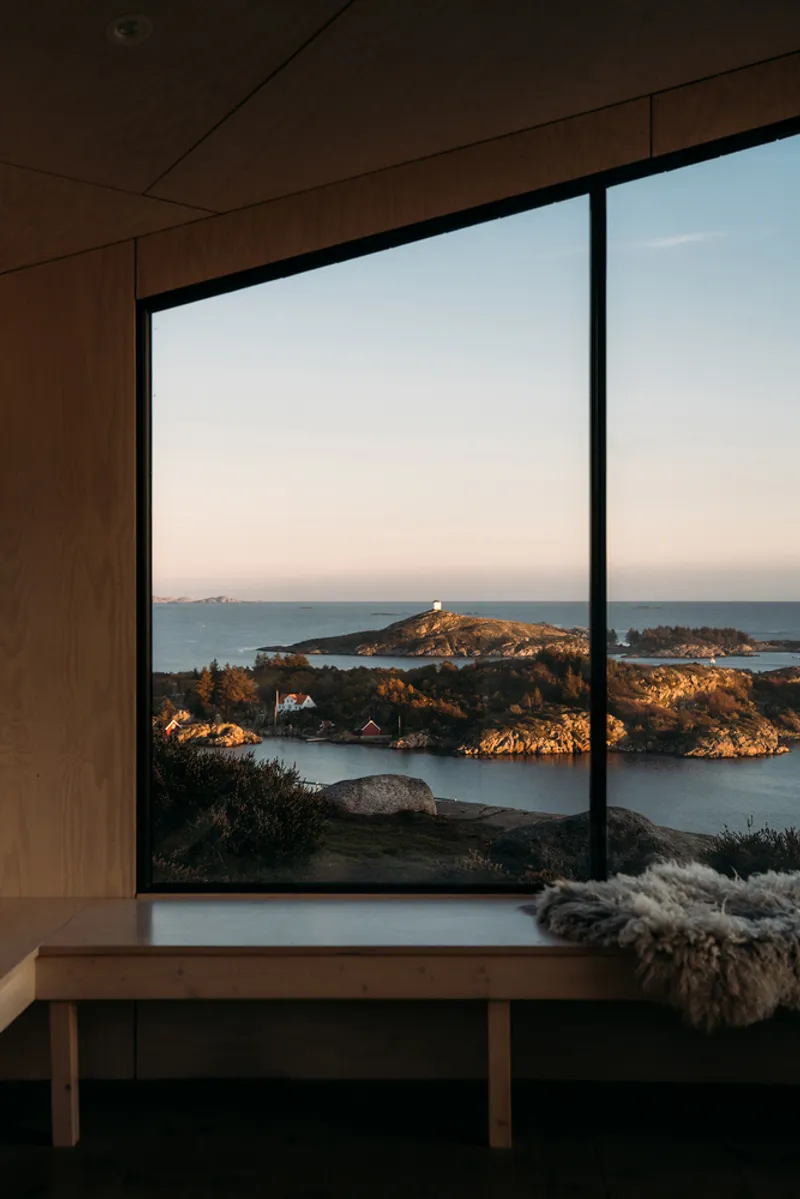 Floor-to-ceiling window framing coastal islands and rocky shoreline in evening light