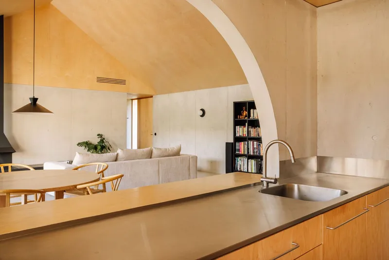Open kitchen with timber cabinetry and stainless steel countertop beneath arched plywood ceiling with recessed vent grille