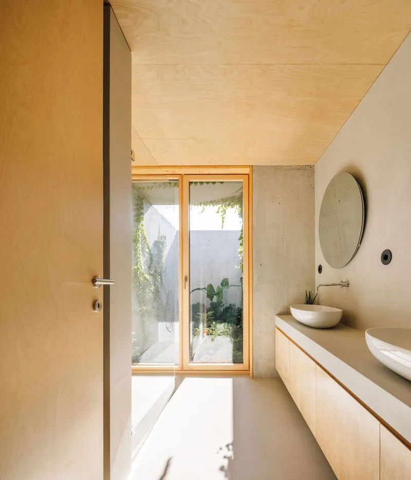 Bathroom with plywood ceiling and timber-framed window opening to a planted courtyard with cacti