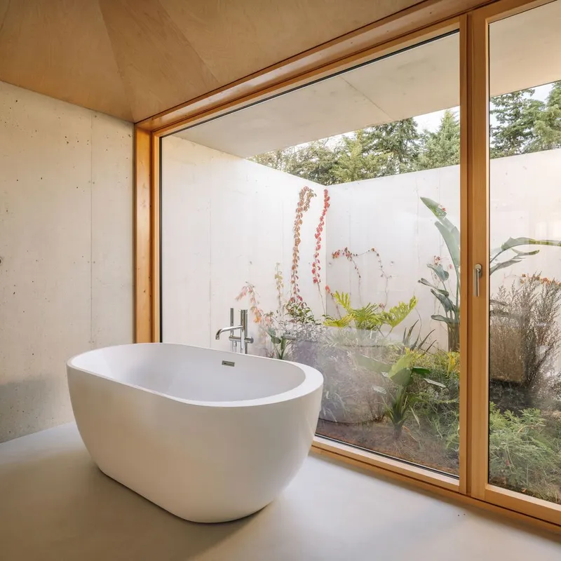 Freestanding bathtub beside timber-framed sliding doors opening to a planted courtyard with banana palms