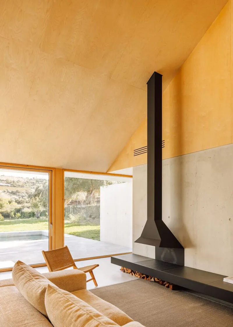Black steel fireplace against concrete wall beneath a vaulted plywood ceiling in warm afternoon light