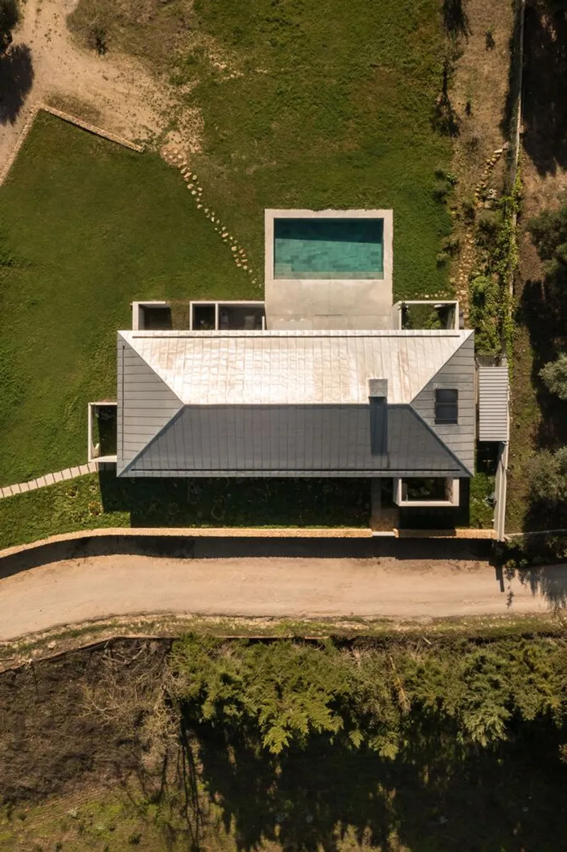Aerial view of the white horizontal volumes with rooftop pool surrounded by green lawn and trees