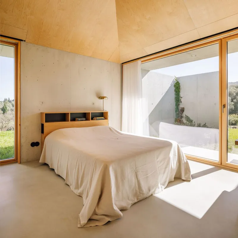 Bedroom with timber-framed glazing opening to a private courtyard with climbing vines