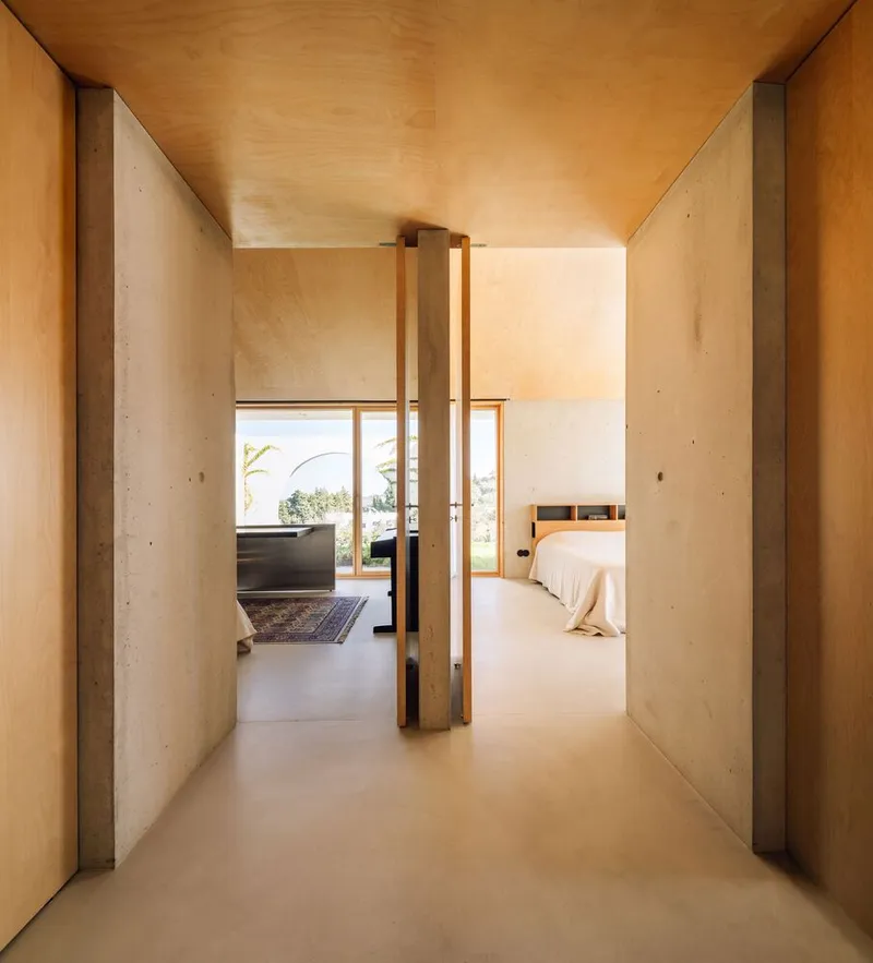 Hallway with timber-framed door, concrete walls, and plywood ceiling leading to bedroom suite