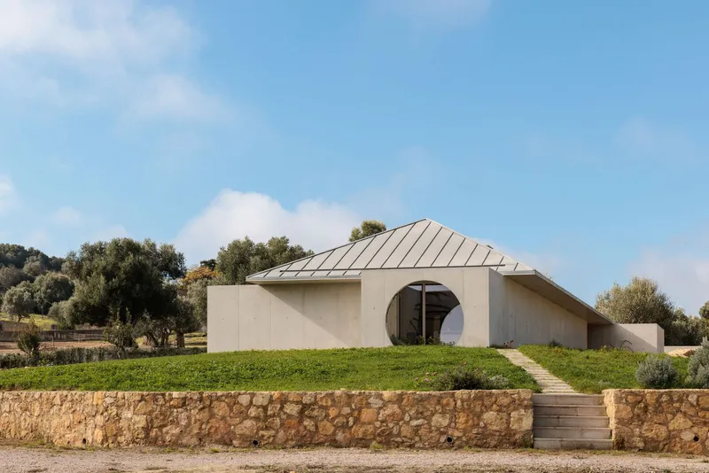 Facade with circular opening and stone retaining wall fronted by timber steps ascending the lawn