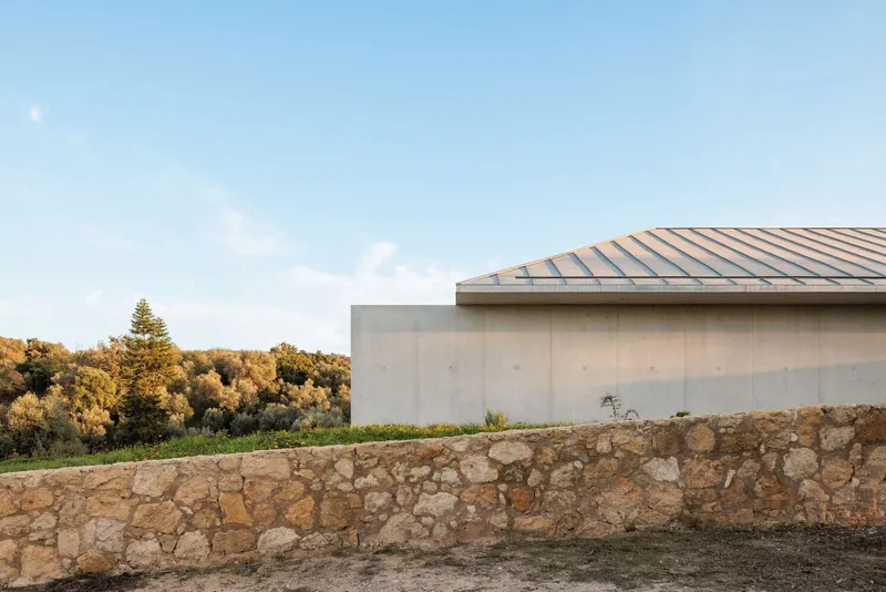 Metal standing seam roof edge above concrete wall with stone retaining wall in afternoon light