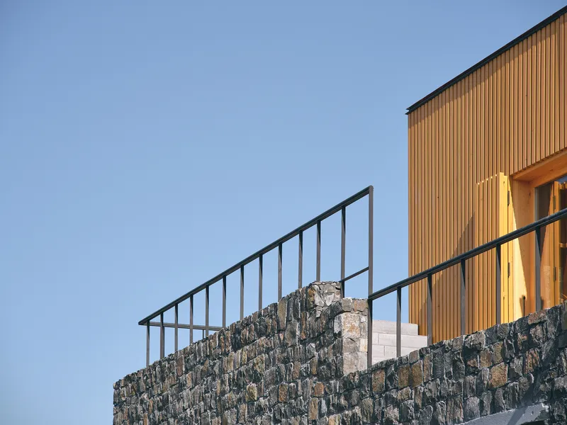 Detail of the steel railing atop a dark stone wall with vertical timber cladding beyond