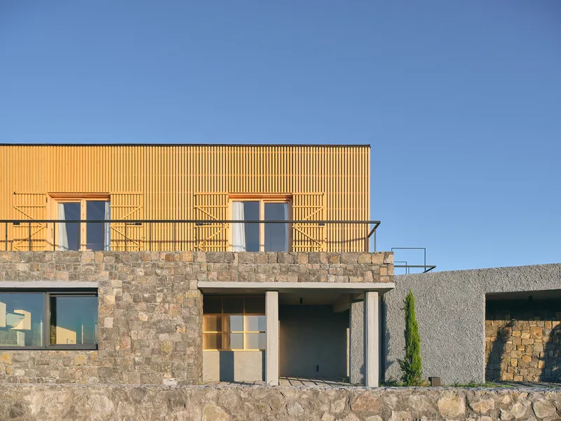 Stone and timber facade with vertical wood cladding and rooftop terrace under a clear blue sky
