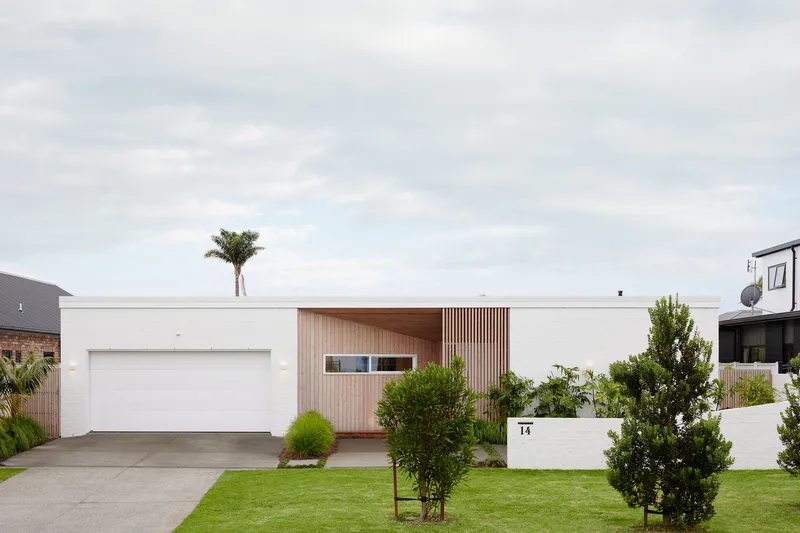 Street view of white brick facade with vertical timber cladding and front lawn with palm tree